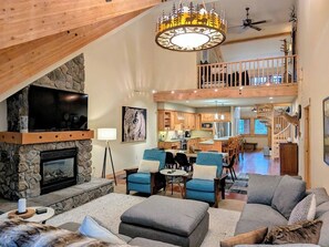 A spacious living area with a stone fireplace, a large television, and a dining area with blue chairs. - Grand Lodge 30 at the Official Collins Lake Resort (Government Camp)