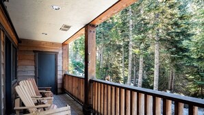 Una terraza de madera con sillas Adirondack, un muro de piedra y vista a un bosque.