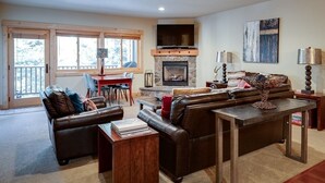 Una sala de estar acogedora con chimenea, sofás de cuero, una mesa de comedor y un televisor sobre la chimenea.