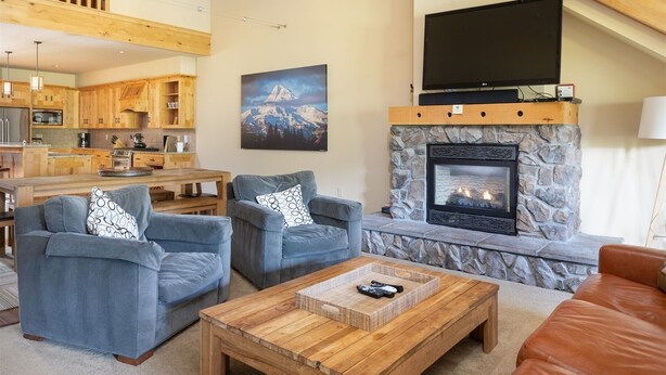 Ein geräumiges Wohnzimmer mit Kamin aus Stein, einem flachbildfernseher darüber und einer gemütlichen Sitzecke mit zwei Sofas und einem Couchtisch.