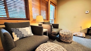 Ein gemütliches Wohnzimmer mit Sofa, Sessel, Hocker und einer Lampe.