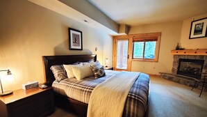 Ein Schlafzimmer mit einem großen Bett, einem Nachttisch, einem Kamin und einem Fenster mit Jalousien.