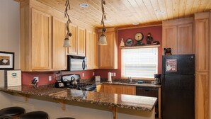 Une cuisine avec des meubles en bois, un plan de travail en granit, un réfrigérateur noir et une cuisinière.
