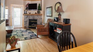 Un salon chaleureux avec une cheminée en pierre, un téléviseur, une horloge et un coin repas comprenant une table et des chaises.