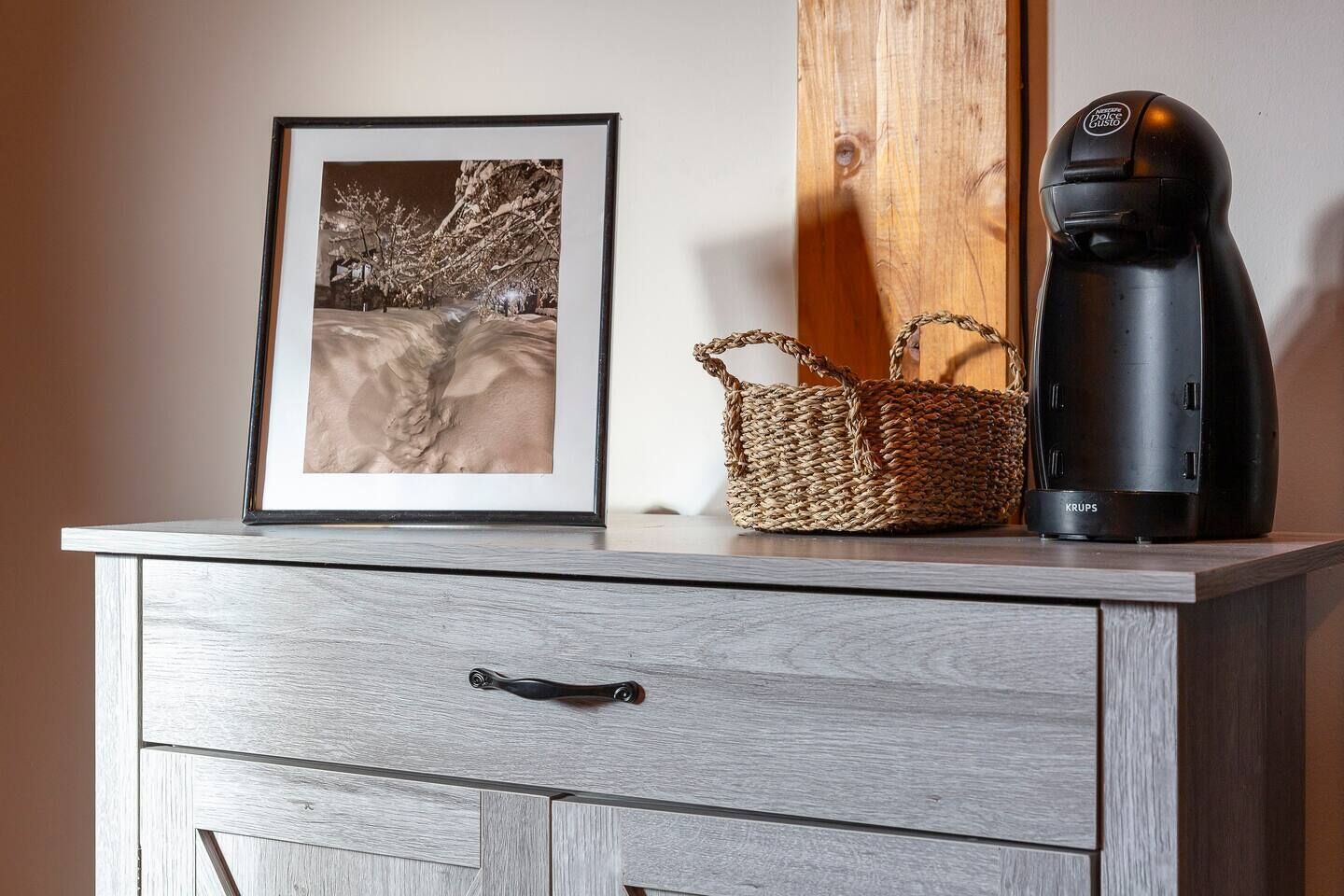 A wooden cabinet with a framed picture, a woven basket, and a black coffee maker.