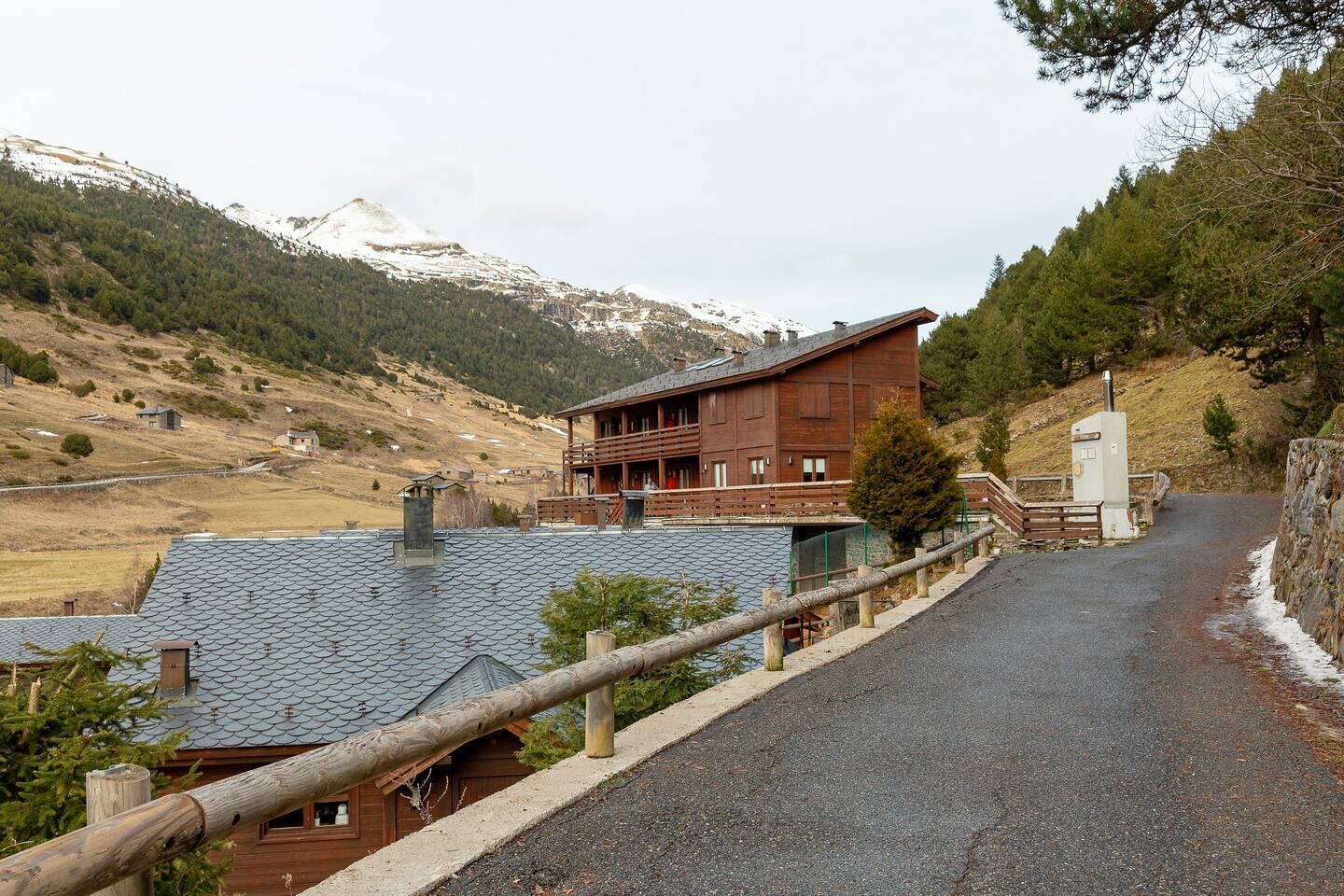 Un albergue de montaña con fachada de madera, un balcón y vistas a montañas nevadas.