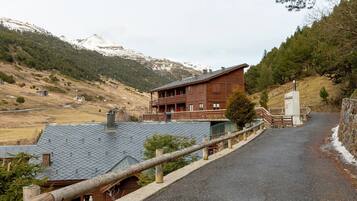 Un albergue de montaña con fachada de madera, un balcón y vistas a montañas nevadas.