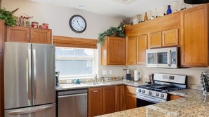 Una cocina con armarios de madera, un refrigerador de acero inoxidable, un microondas, una estufa y encimeras de granito.