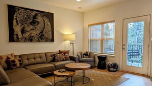 A living room with a sectional sofa, a round coffee table, a lamp, and a large painting of an owl. - Chalet 73 at the Official Collins Lake Resort (Government Camp)