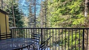 A balcony with a metal table and chairs, overlooking a forested area. - Chalet 73 at the Official Collins Lake Resort (Government Camp)