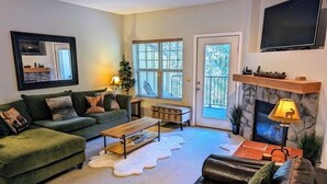 A living room with a green sofa, a black leather couch, a wooden coffee table, and a fireplace. - Chalet 75 at the Official Collins Lake Resort (Government Camp)