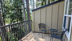 A wooden deck with a metal railing, two chairs, and a small table.