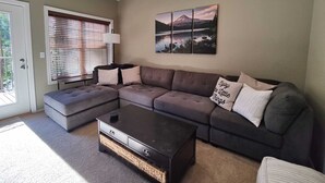 A living room with a sectional sofa, a coffee table, and a wall-mounted artwork.