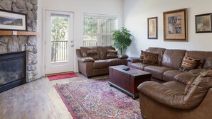 Una sala de estar con pared de piedra, dos sofás de cuero, una mesa de centro, una chimenea y una alfombra grande.