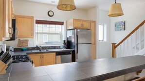Una cocina moderna con armarios de madera, un refrigerador de acero inoxidable, un horno integrado y una isla grande con azulejos grises.