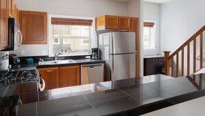 A modern kitchen with wooden cabinets, a stainless steel refrigerator, a gas stove, and a dishwasher. - Chalet 133 at the Official Collins Lake Resort (Government Camp)