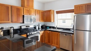 A modern kitchen with wooden cabinets, stainless steel appliances, a black countertop, and a window with blinds. - Chalet 133 at the Official Collins Lake Resort (Government Camp)