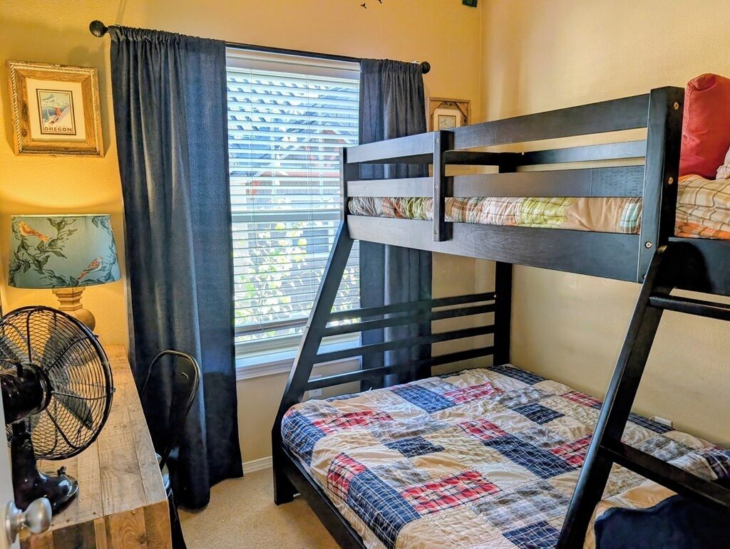 A bunk bed room with a window, curtains, a fan, and a framed picture on the wall.
