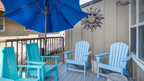 Une terrasse avec des fauteuils Adirondack turquoise, un parasol bleu et une décoration murale en forme de soleil.