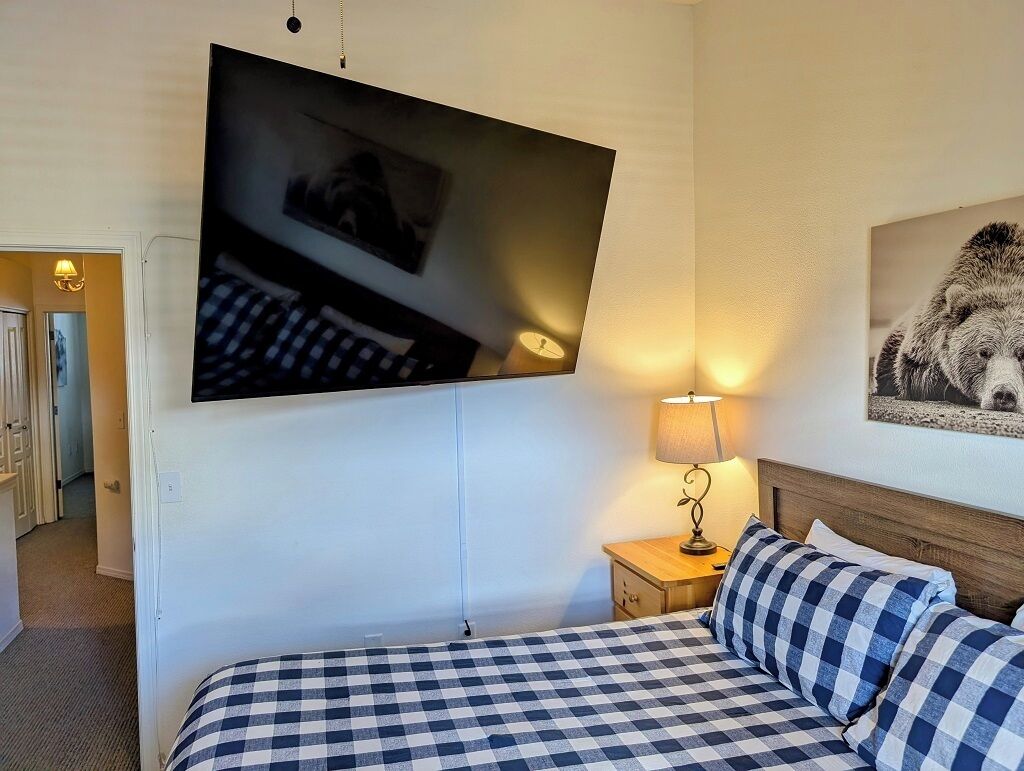 A hotel room with a bed, a TV mounted on the wall, a bedside lamp, and a framed picture on the wall.