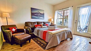Un dormitorio con cama, una silla, una alfombra y una ventana con cortinas.
