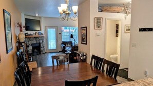 A dining area with a large wooden table and chairs, a chandelier, and a television mounted on the wall. - Chalet 35 at the Official Collins Lake Resort (Government Camp)