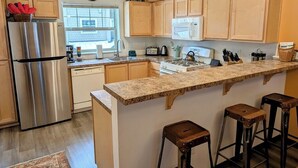 A modern kitchen with wooden cabinets, stainless steel appliances, a granite countertop, and a bar stool area. - Chalet 35 at the Official Collins Lake Resort (Government Camp)