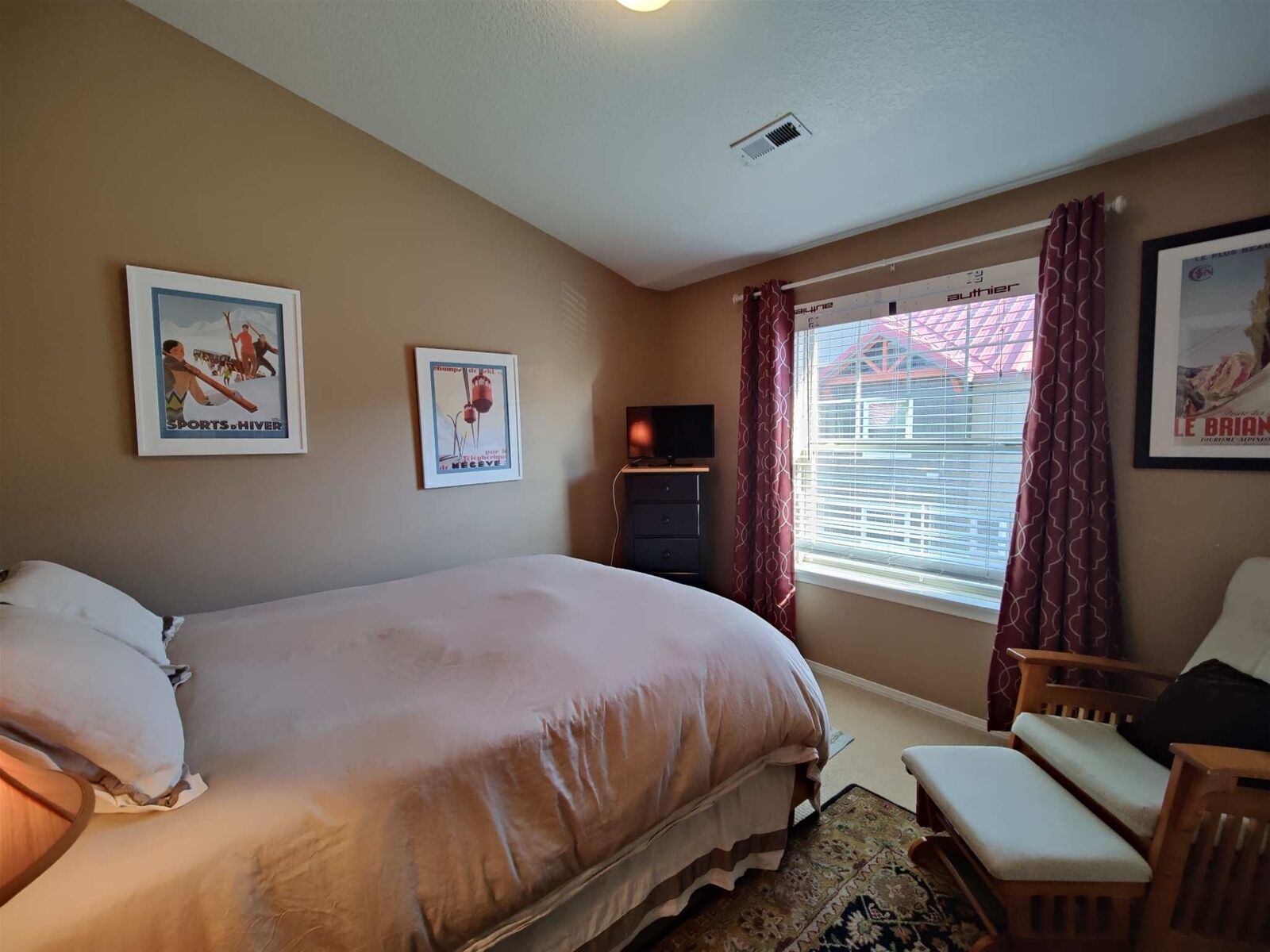 A bedroom with a bed, a chair, a TV, and two posters on the wall.