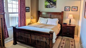 Une chambre à coucher avec un lit en bois, une table de chevet avec une lampe, une fenêtre avec des rideaux et un tableau accroché au mur.