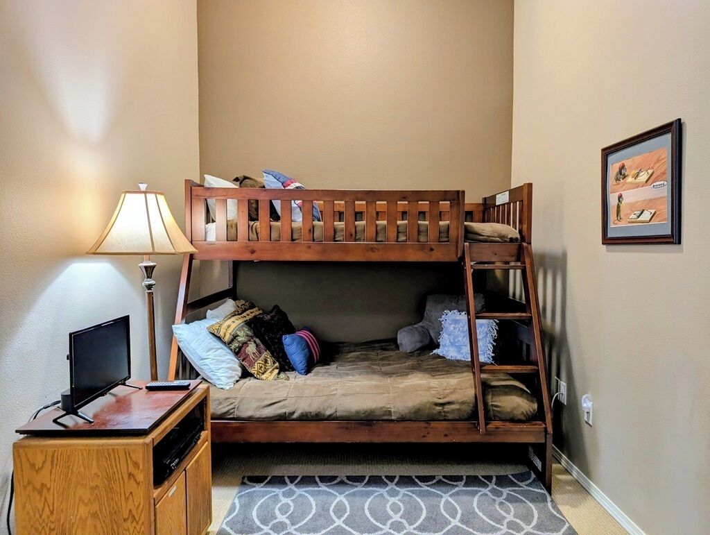 A bunk bed with a TV stand, a desk, and a lamp.