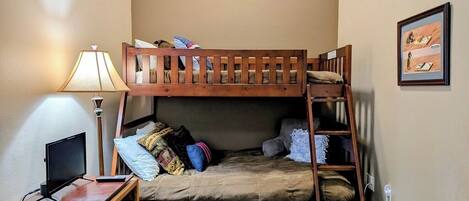 A bunk bed with a TV stand, a desk, and a lamp.