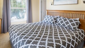Un dormitorio con una colcha estampada, un cabecero de madera, una ventana con cortinas y un cuadro en la pared.
