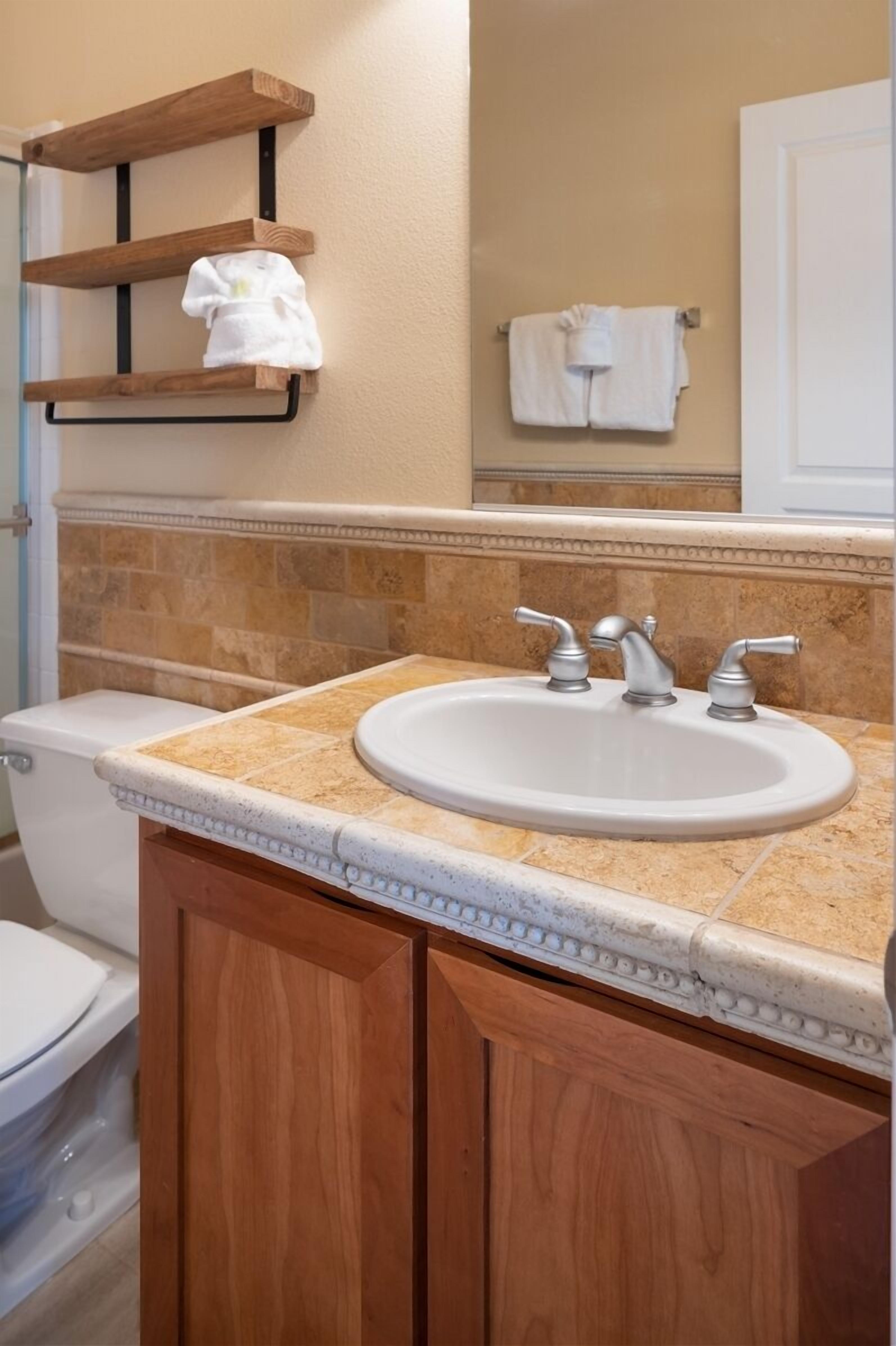 A bathroom with a white sink, wooden cabinets, and a beige tiled backsplash.