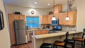 Una cocina moderna con armarios de madera, electrodomésticos de acero inoxidable, una isla central con taburetes de bar y una ventana con persianas.