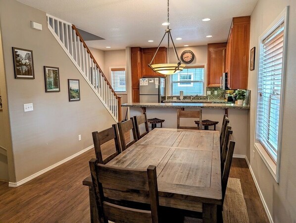 Un comedor con una mesa y sillas de madera, una cocina con armarios de madera y un refrigerador, y una escalera que conduce a otro nivel.
