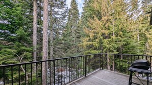 A deck with a metal railing overlooking a forested area with tall trees. - Chalet 103 at the Official Collins Lake Resort (Government Camp)