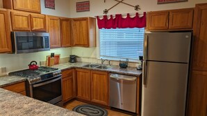 A kitchen with wooden cabinets, a stainless steel refrigerator, a microwave, a stove, and a sink. - Chalet 103 at the Official Collins Lake Resort (Government Camp)