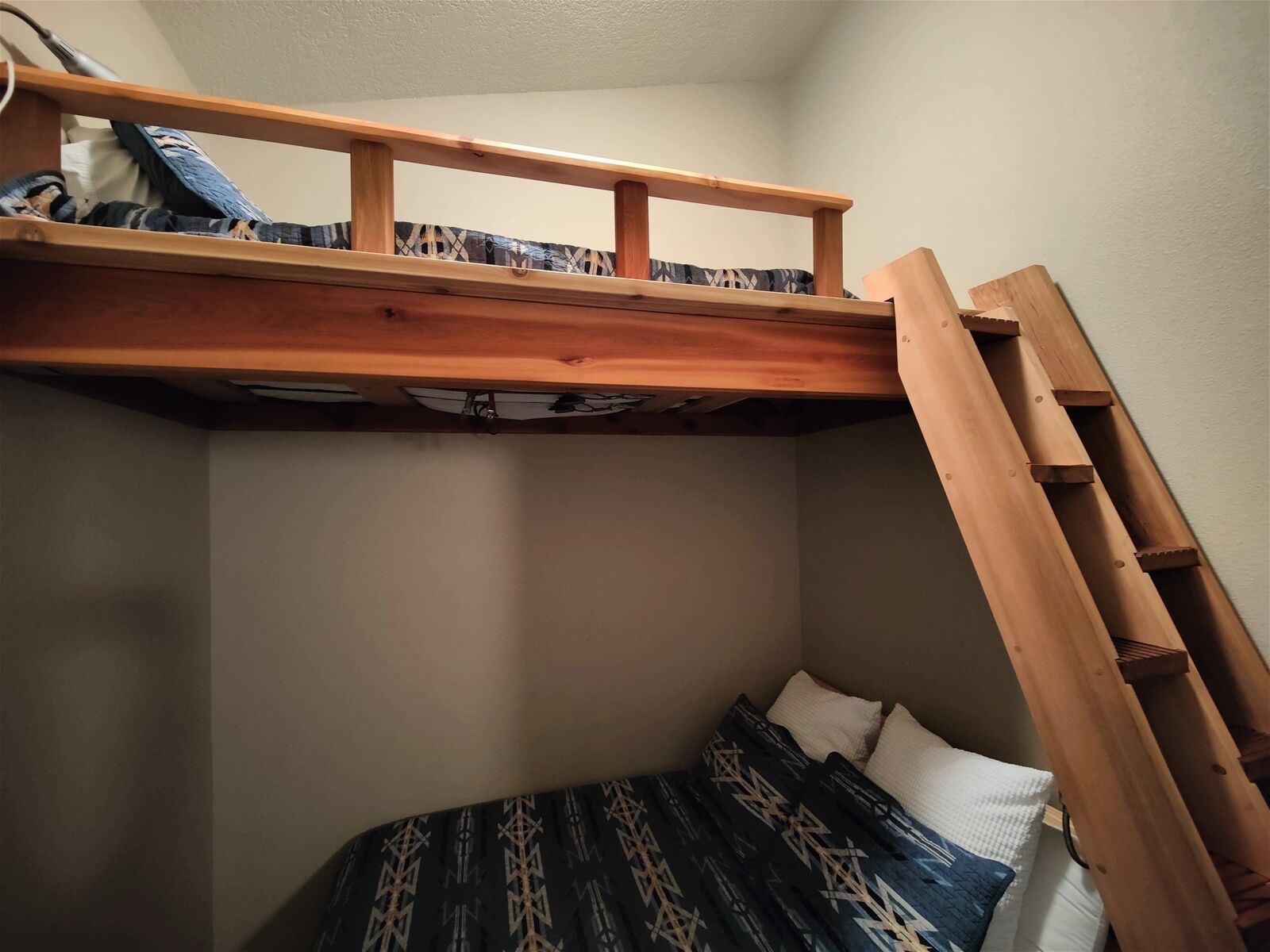 A bunk bed with a wooden ladder, a patterned blanket, and pillows.