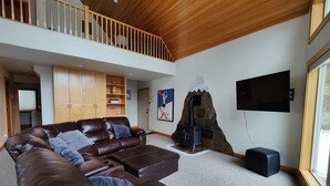 A spacious living room with a brown leather sofa, a stone fireplace, a television mounted on the wall, and a wooden ceiling. - Slope Side Cabin at the Official Collins Lake Resort (Government Camp)