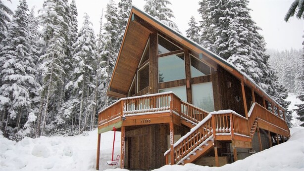 A wooden cabin with a large glass window, a wooden deck, and a staircase leading to the entrance. - Slope Side Cabin at the Official Collins Lake Resort (Government Camp)
