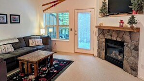 A living room with a fireplace, a sofa, a coffee table, and a television mounted above the fireplace.
