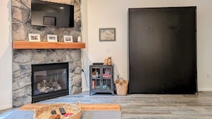 Un salon doté d’une cheminée en pierre, d’un téléviseur à écran plat fixé au-dessus, d’une porte sombre et d’une petite armoire sur laquelle sont posés divers objets.