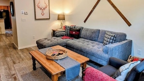 Un salon chaleureux avec un canapé d’angle, une table basse en bois et une paire de skis accrochés au mur.