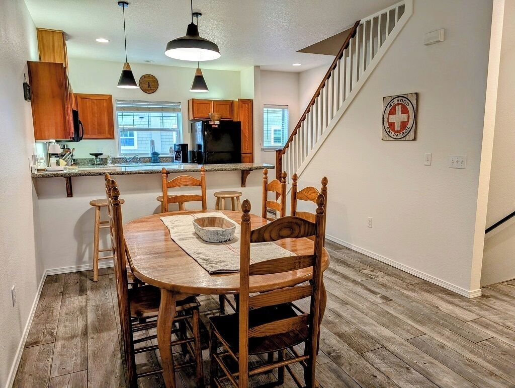 Un comedor con una mesa y sillas de madera, una cocina al fondo y una escalera que sube.