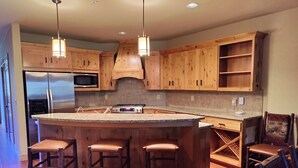 A kitchen with wooden cabinets, stainless steel appliances, a large island with stools, and pendant lighting.
