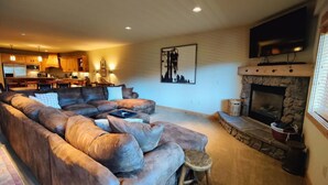 A cozy living room with a large sectional sofa, a fireplace, and a kitchen in the background.