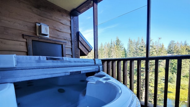 A hot tub on a wooden deck with a view of a forest and a lake.