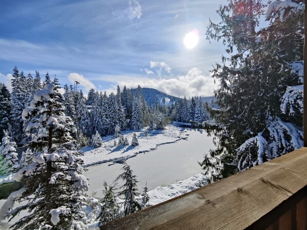 A snowy landscape with a lake, trees, and a wooden deck.