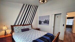 A bedroom with a bed, nightstand, lamp, and a door leading to another room. - Chalet 32 at the Official Collins Lake Resort (Government Camp)