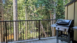 A balcony with a grill, surrounded by tall trees.